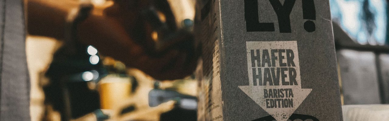 Eine Oatly-Hafermilch steht vor der Siebträgermaschine, während Kaffee zubereitet wird.