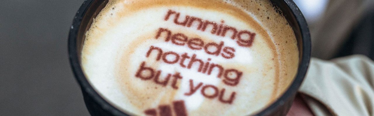 Auf einem Kaffee steht im Schaum "running needs nothing but you". Darunter das Adidas-Logo.